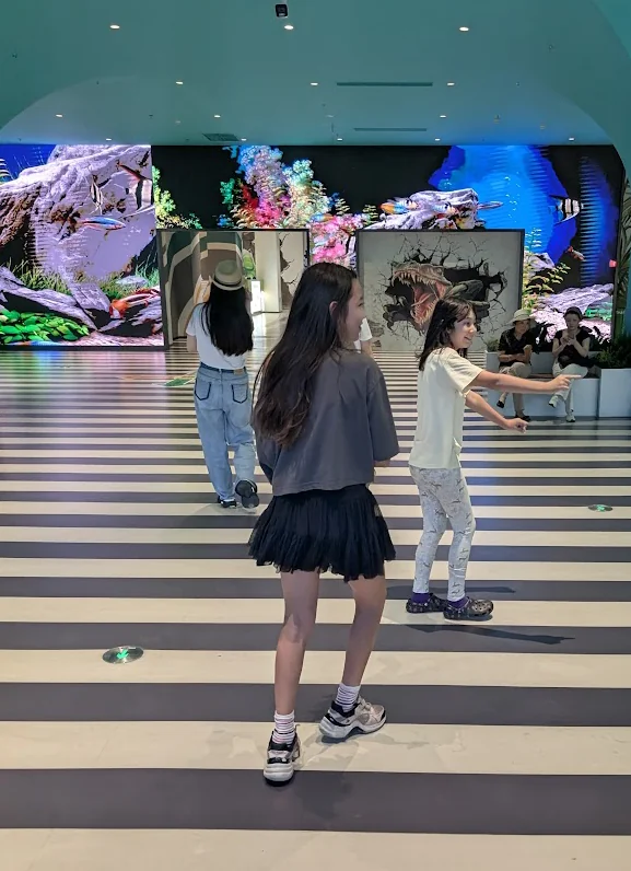 The girls walking through a hall of glowing dinosaur murals