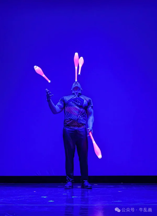 A juggler with glowing clubs under deep blue light
